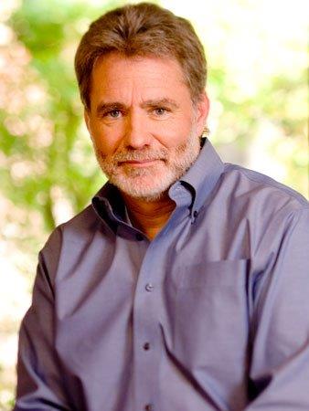 A man in a blue shirt smiling outdoors.